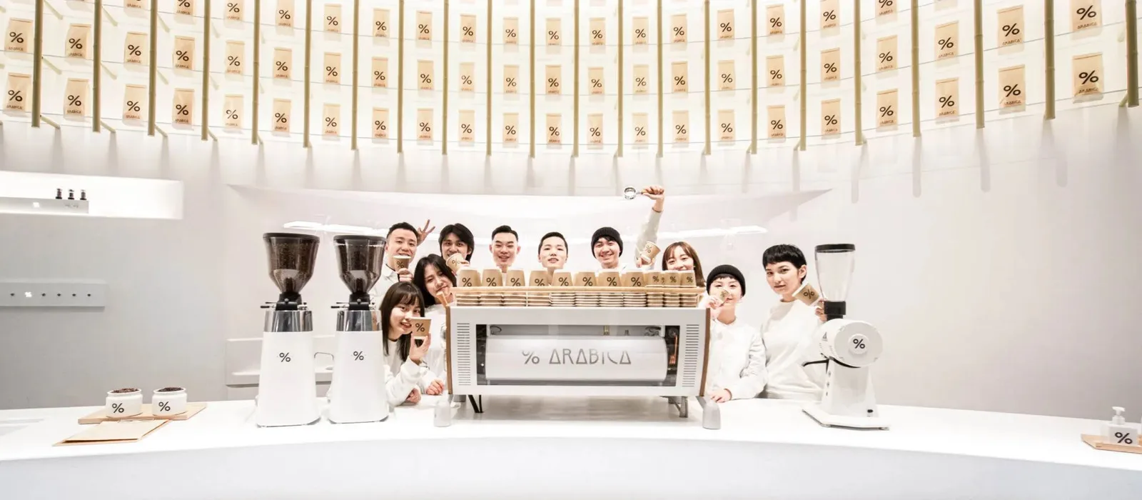 team poses behind espresso machine in minimalist white café with percentage symbols., 杰森咖啡烘焙工坊, chengdu