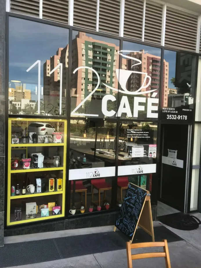 storefront café with yellow shelving display, large windows, and sandwich board sign., 112 café, brasília