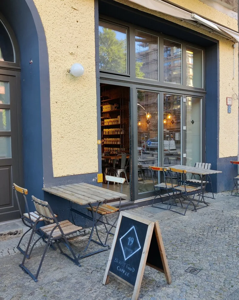 modern café storefront with outdoor seating and wooden tables on cobblestone street., 19grams chaussee, berlin