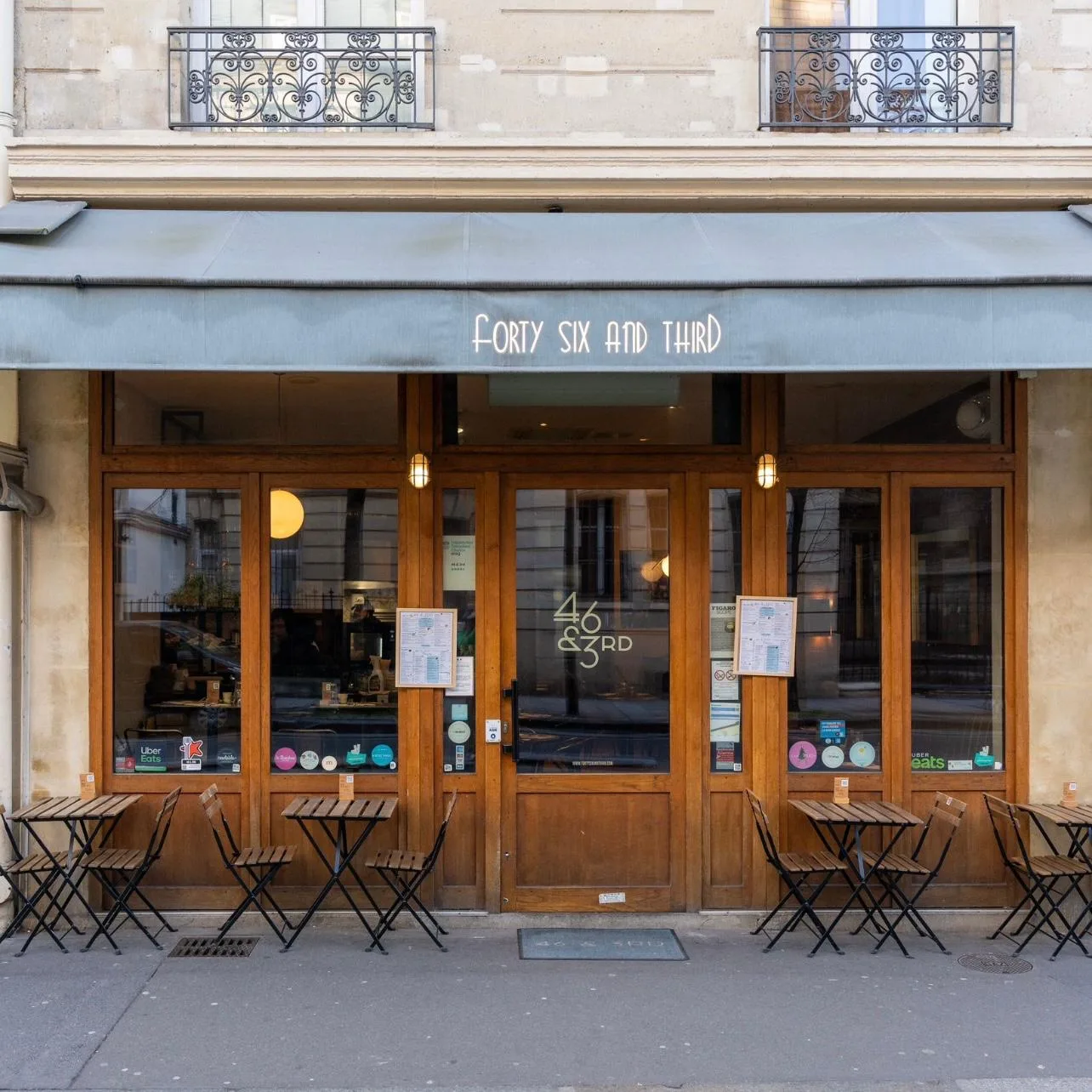 parisian storefront with wooden doors, outdoor seating, and ornate balconies above., 46 & 3rd - forty six and third, paris