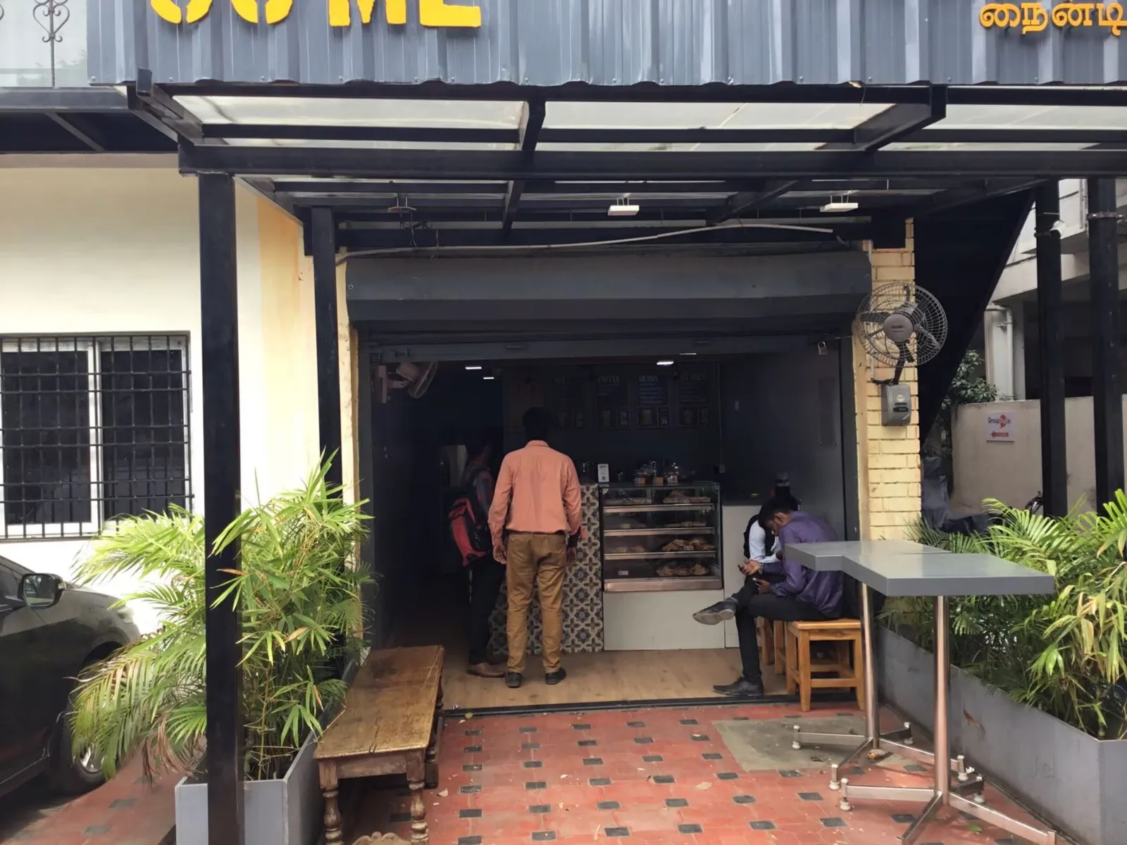 small shopfront cafe with counter service, plants, and seated customer., 90ml, chennai