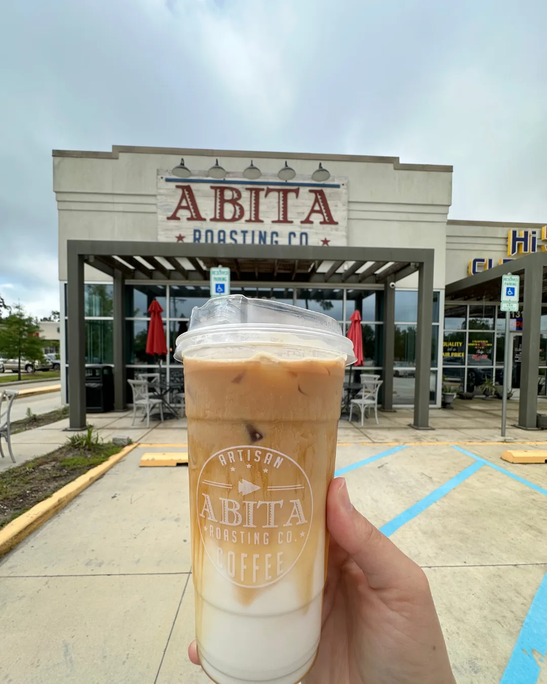 iced coffee drink held in front of abita roasting co. storefront exterior., abita roasting company, covington