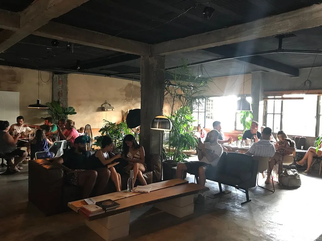 industrial loft space with multiple groups seated, plants, concrete floors, natural light., acervo café & roastery, brasília