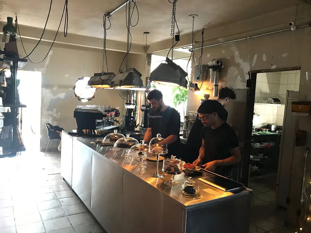 coffee shop interior with three baristas working behind counter under pendant lights., acervo café & roastery, brasília