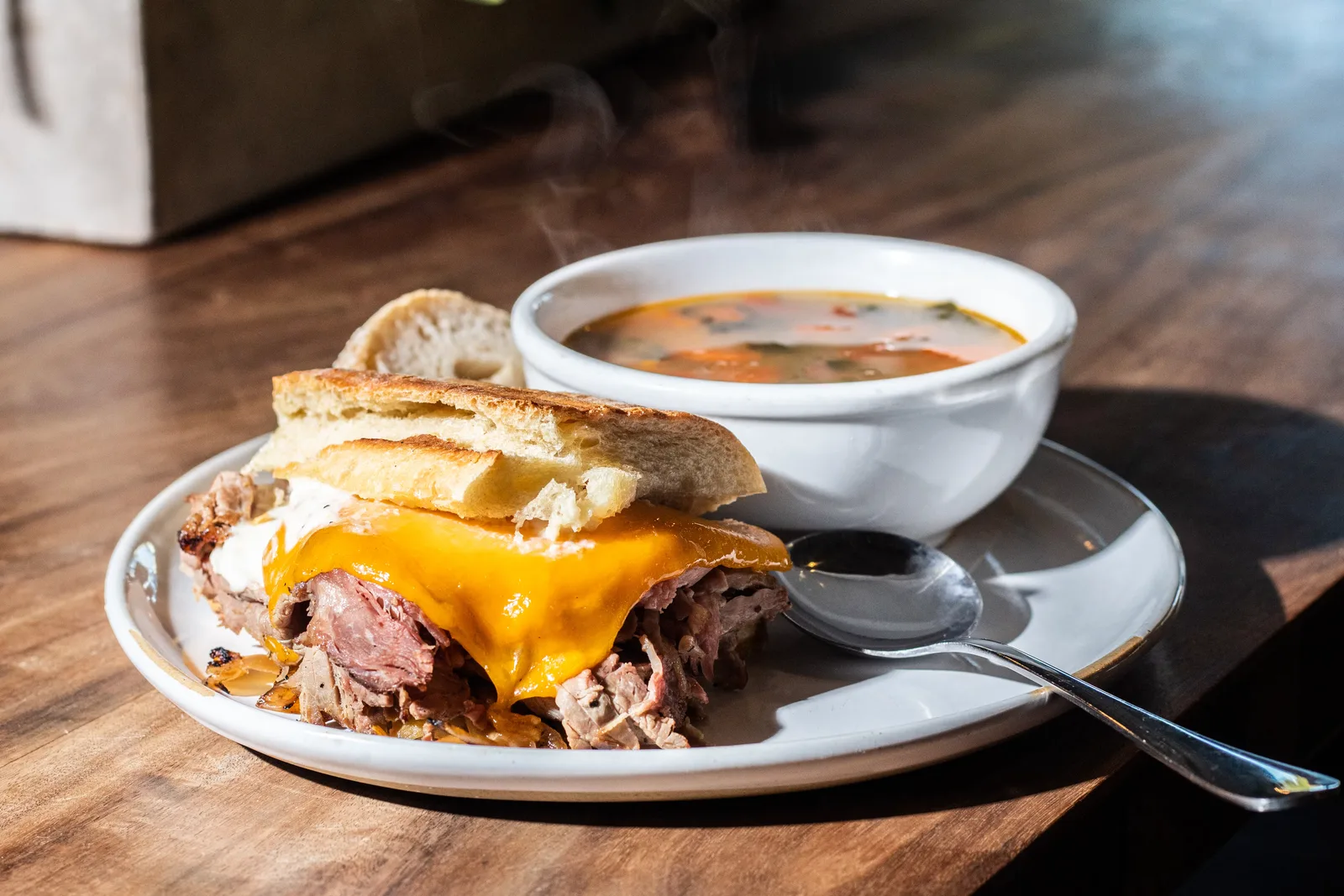 roast beef sandwich with melted cheddar cheese and soup on wooden table., aioli, miami