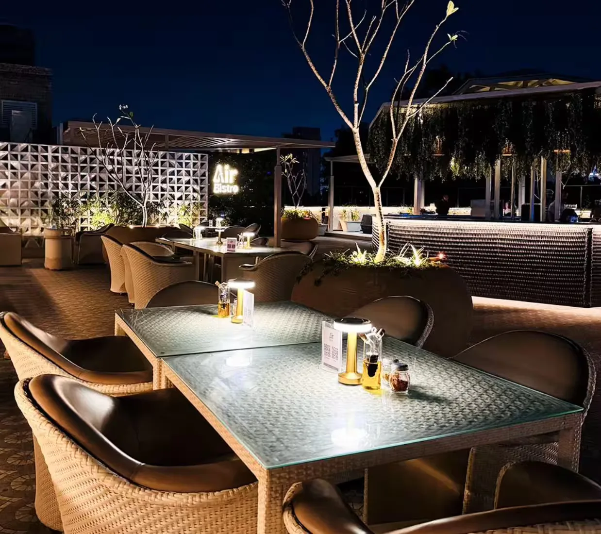 upscale rooftop dining area with woven chairs and illuminated trees at night., air bistro, ahmedabad