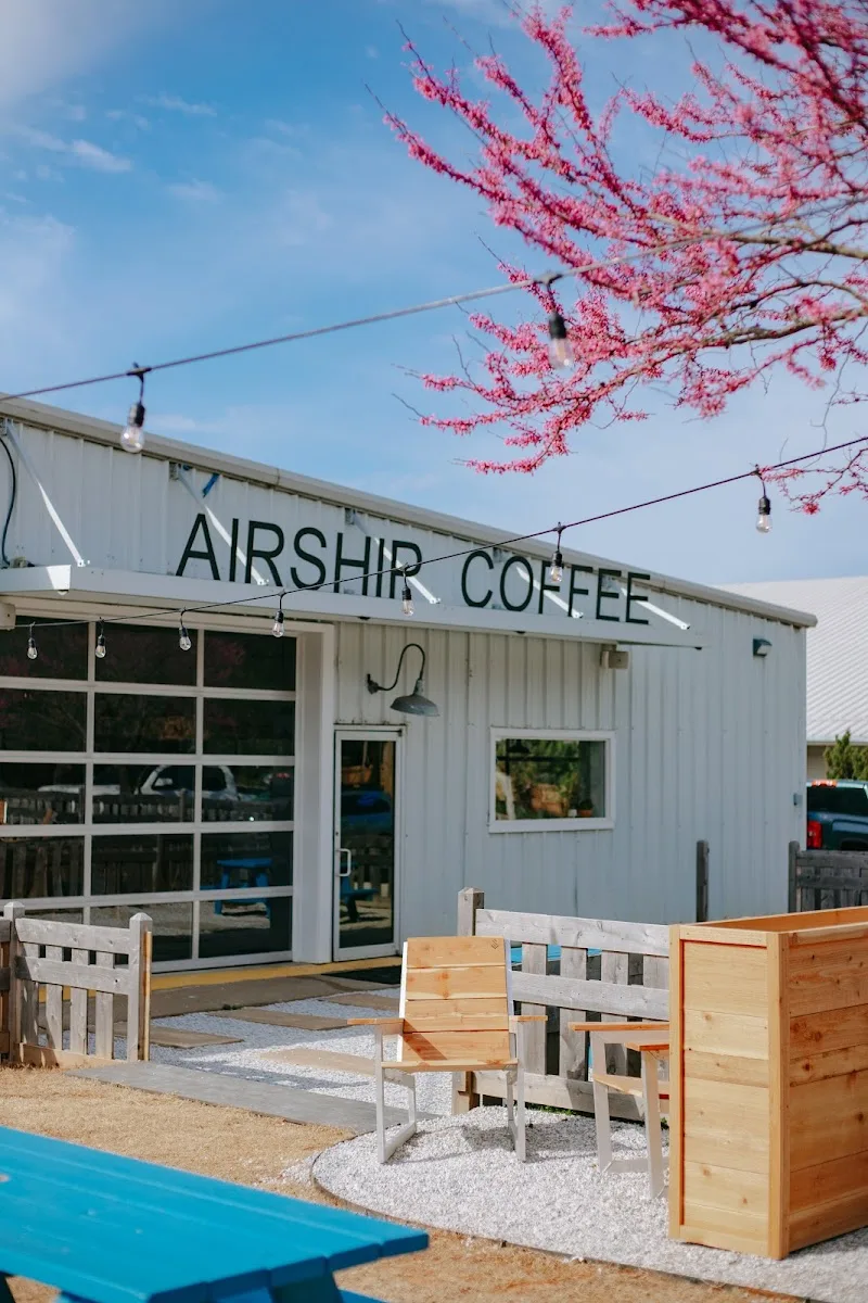 modern coffee shop with pink flowering tree, wooden seating, and blue sky., airship coffee at 5th street, bentonville