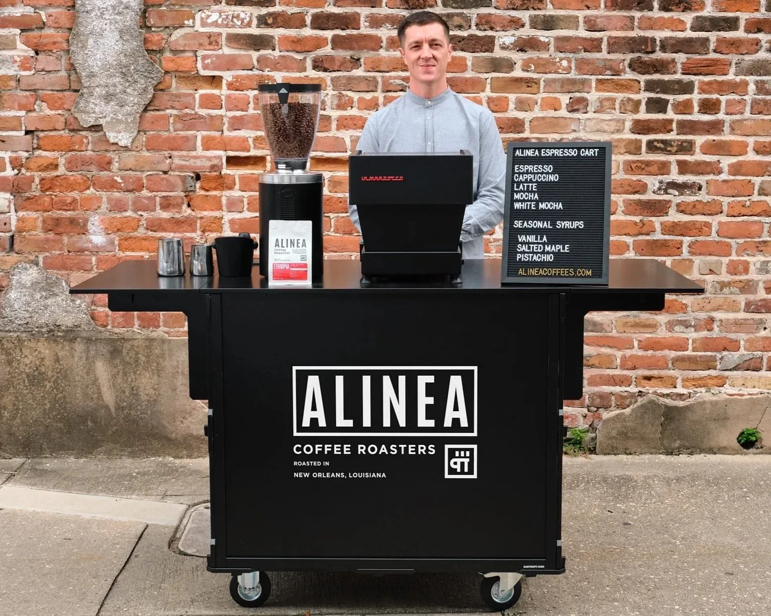 man operates alinea coffee roasters cart against brick wall backdrop., alinea coffee roasters, new orleans