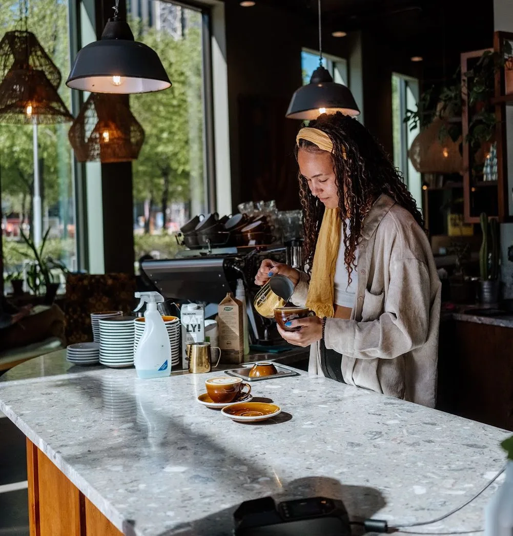 woman pouring coffee at marble counter in modern café with pendant lighting., alkemisten, gothenburg