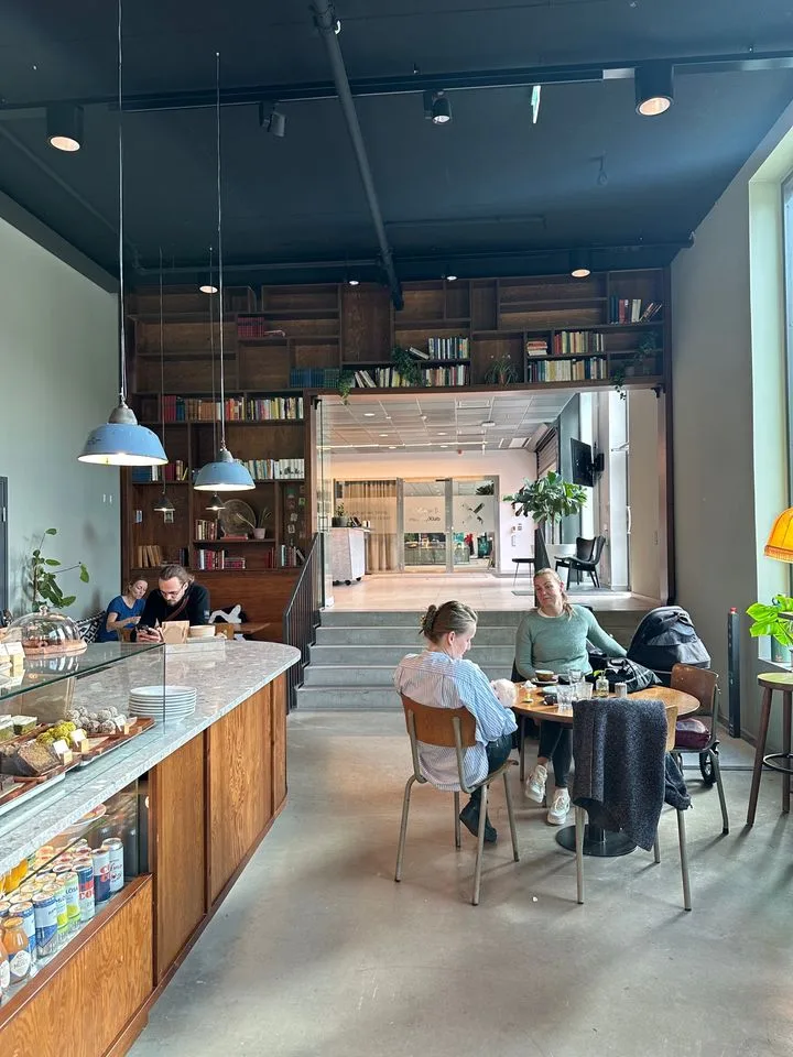 modern café interior with customers, wooden cabinetry, bookshelves, and pendant lighting., alkemisten, gothenburg