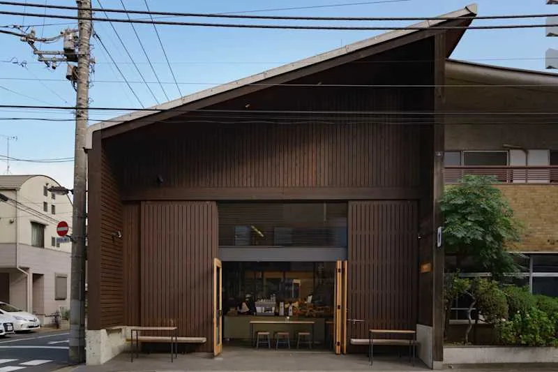 modern brown corrugated metal storefront with open doors and wooden benches outside., allpress espresso tokyo roastery & cafe