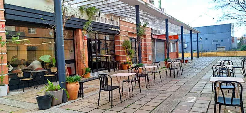 outdoor patio dining area with black chairs, brick buildings, and potted plants., alquimista coffee lab, mairena del aljarafe