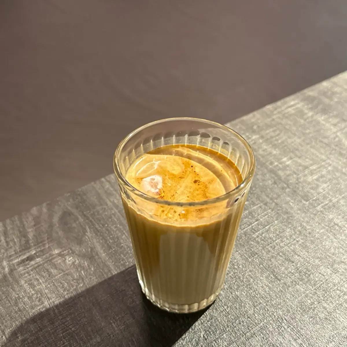 golden milk beverage in ribbed glass on textured gray surface with sunlight., always day one cafe, taipei