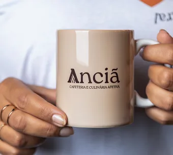 person holding beige ceramic mug with "ancía" branding and spanish text., anciã - cafeteria & culinária afetiva, belo horizon