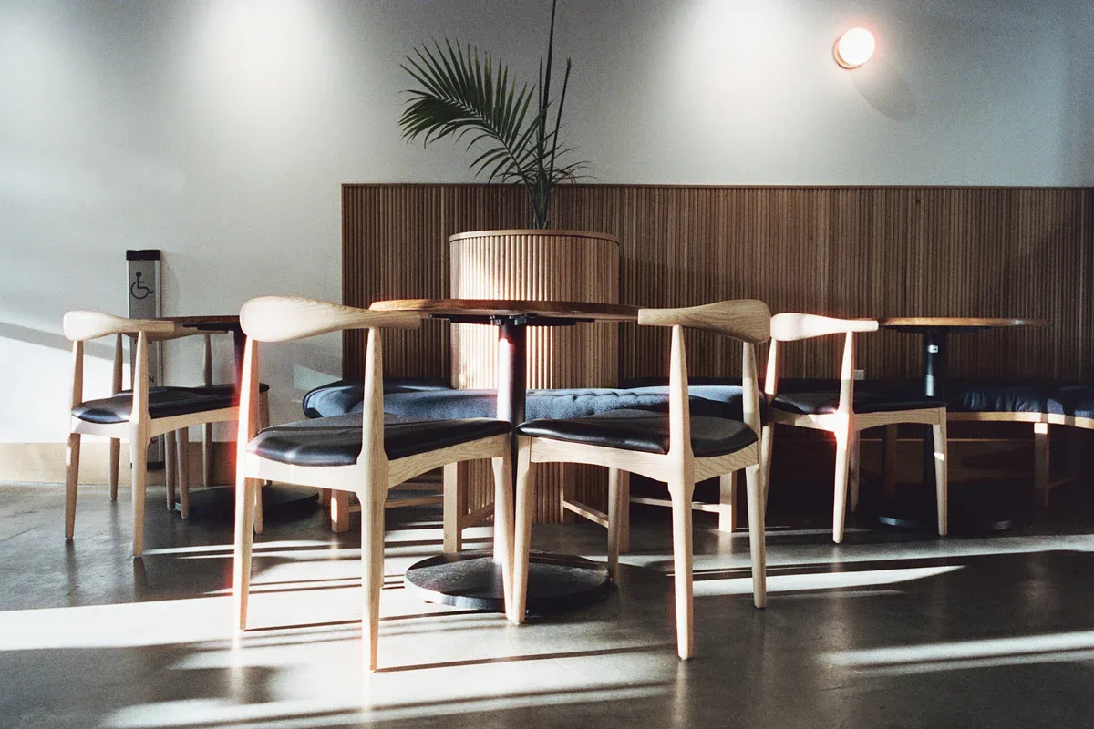 modern dining space with wooden chairs, round table, and potted plant., arcade coffee roasters - tasting room, riverside