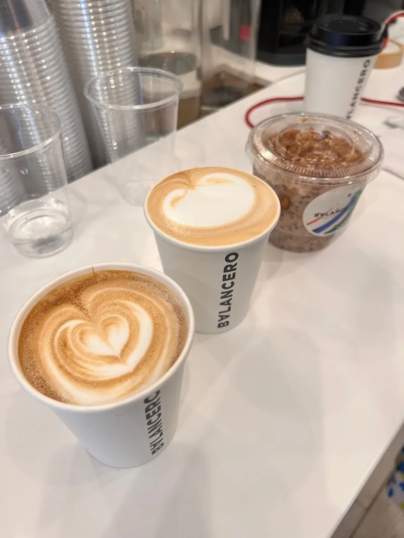 two lattes with latte art beside a cold beverage cup on counter., balancero, new york city