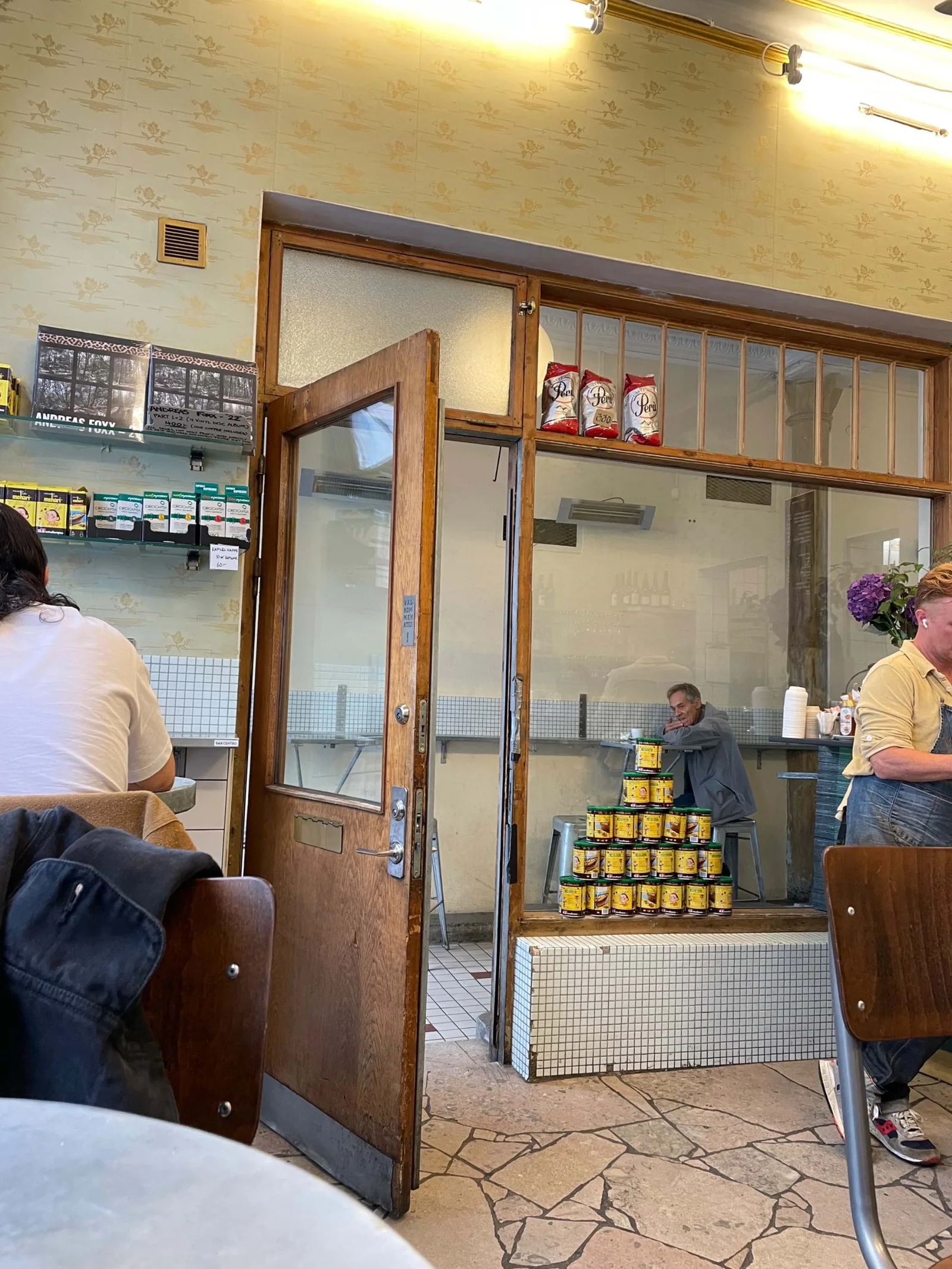 vintage deli interior with wooden doors, customers, and stacked yellow product boxes., bar centro, gothenburg