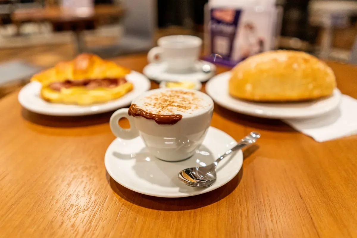 cappuccino with cocoa powder and biscuit beside pastries and bread on wooden table., barbarella bakery, curitiba