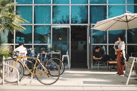yellow bicycle parked outside modern storefront with people seated under umbrellas., basking coffee, fukuoka