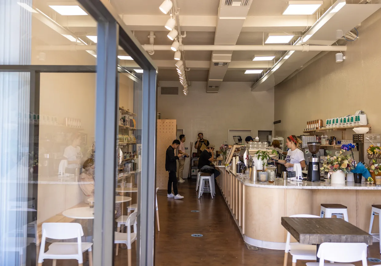 modern minimalist café with light wood counter, potted flowers, and staff preparing beverages., be bright coffee, los angeles