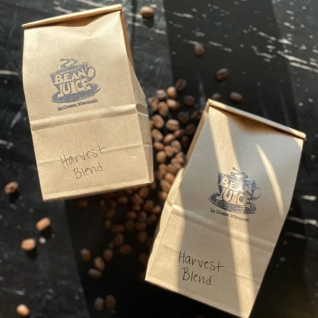 two kraft paper coffee bags labeled "harvest blend" from bean juice, la crosse wisconsin, with scattered coffee beans., bean 
