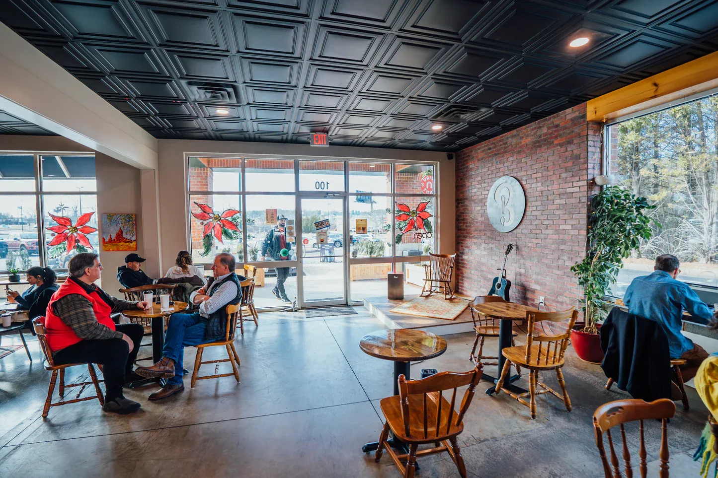 modern café interior with brick walls, wooden chairs, and large front windows displaying holiday decorations., because coffee