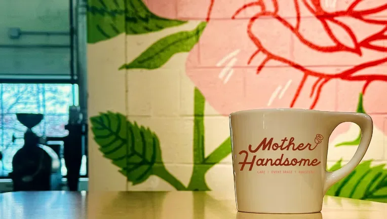 cream mug with "mother handsome" text sits on counter near botanical wall mural., berkley coffee, detroit