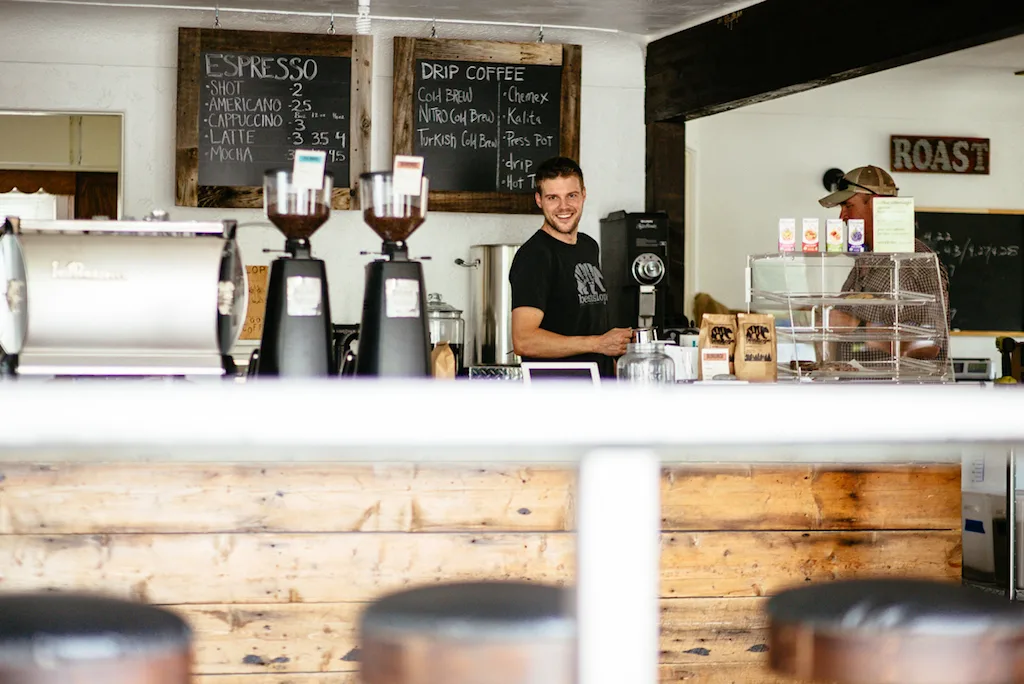 smiling barista at specialty coffee shop counter with menu boards above., bestslope coffee company, fruita