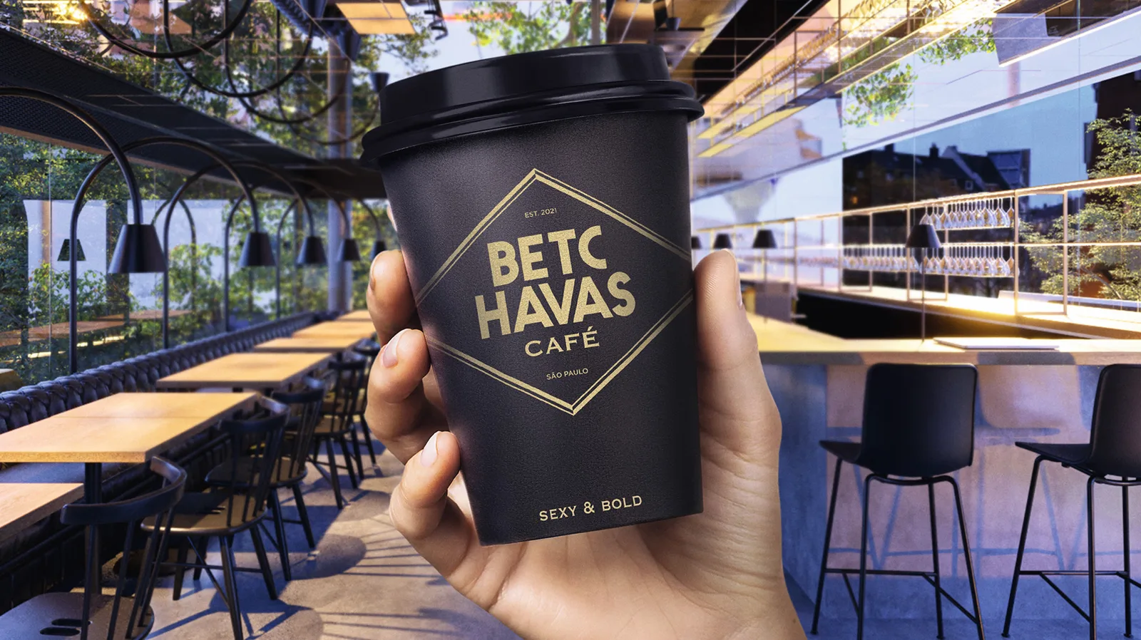 hand holding black coffee cup in modern café setting with plants and seating., betc havas café, são paulo