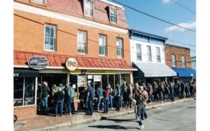 large crowd of people lined up outside brick storefronts on sunny street., bitty and beau’s coffee, charleston