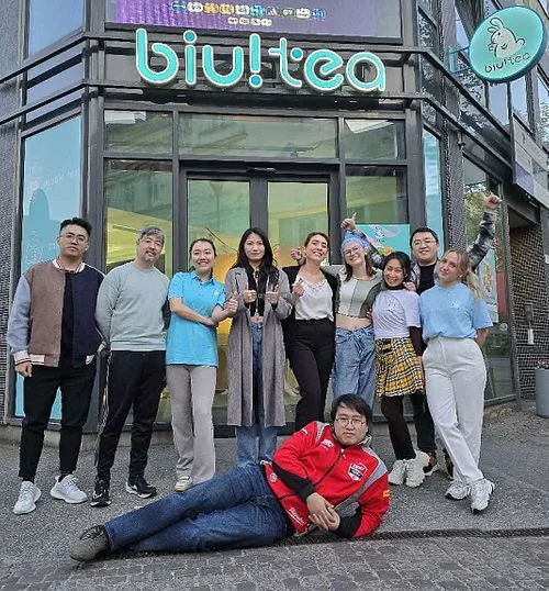 group of people posing outside biutiea storefront, one person lying on ground., biu!tea malmö, malmö
