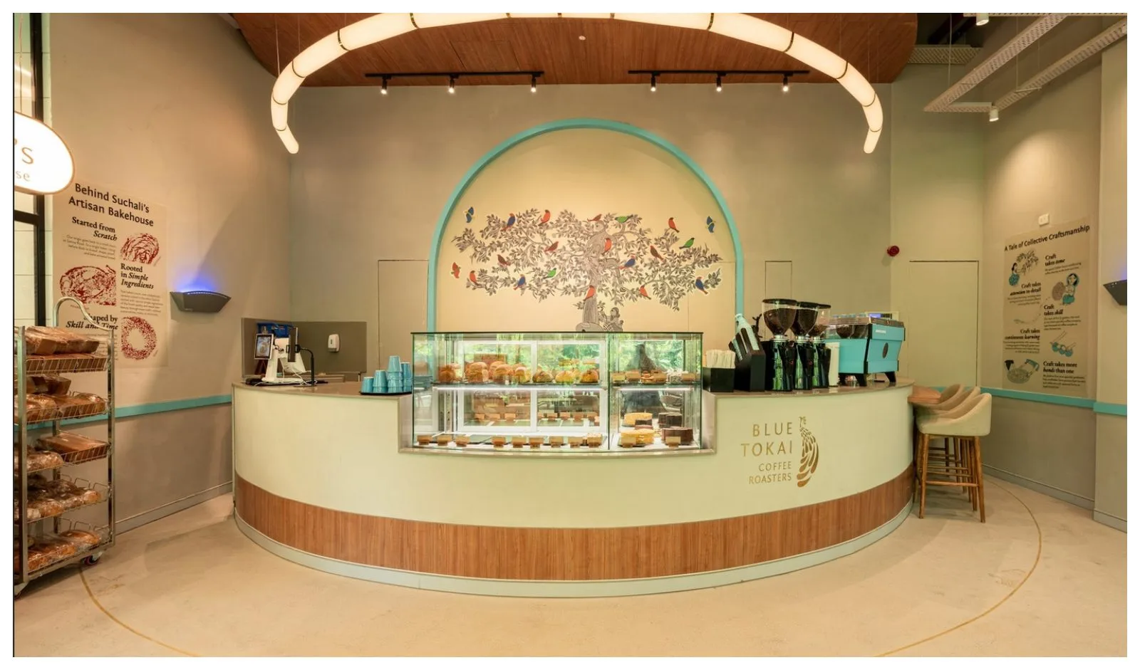 modern bakery and coffee shop with curved counter, pastry display, and decorative bird artwork., blue tokai coffee roasters |