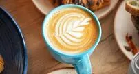 blue coffee cup with latte art on wooden table surrounded by pastries., blue tokai coffee roasters | mohali, sahibzada ajit s