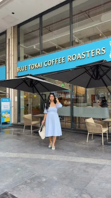 woman in light blue dress stands outside blue tokai coffee roasters storefront., blue tokai coffee roasters | mohali, sahibza