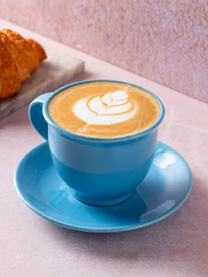blue cup and saucer with latte art, croissant, pink textured background., blue tokai coffee roasters | vasant vihar, new delh