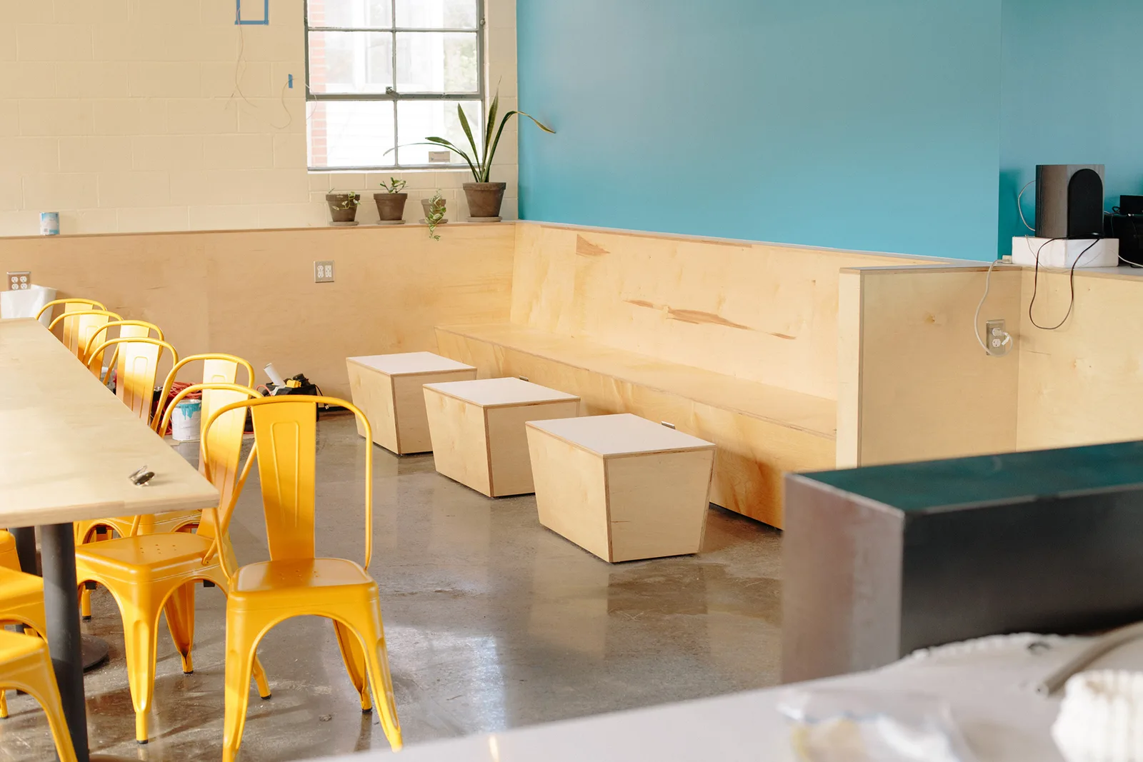 modern cafe interior with yellow chairs, wooden benches, and potted plants by window., blueprint coffee - watson, st. louis