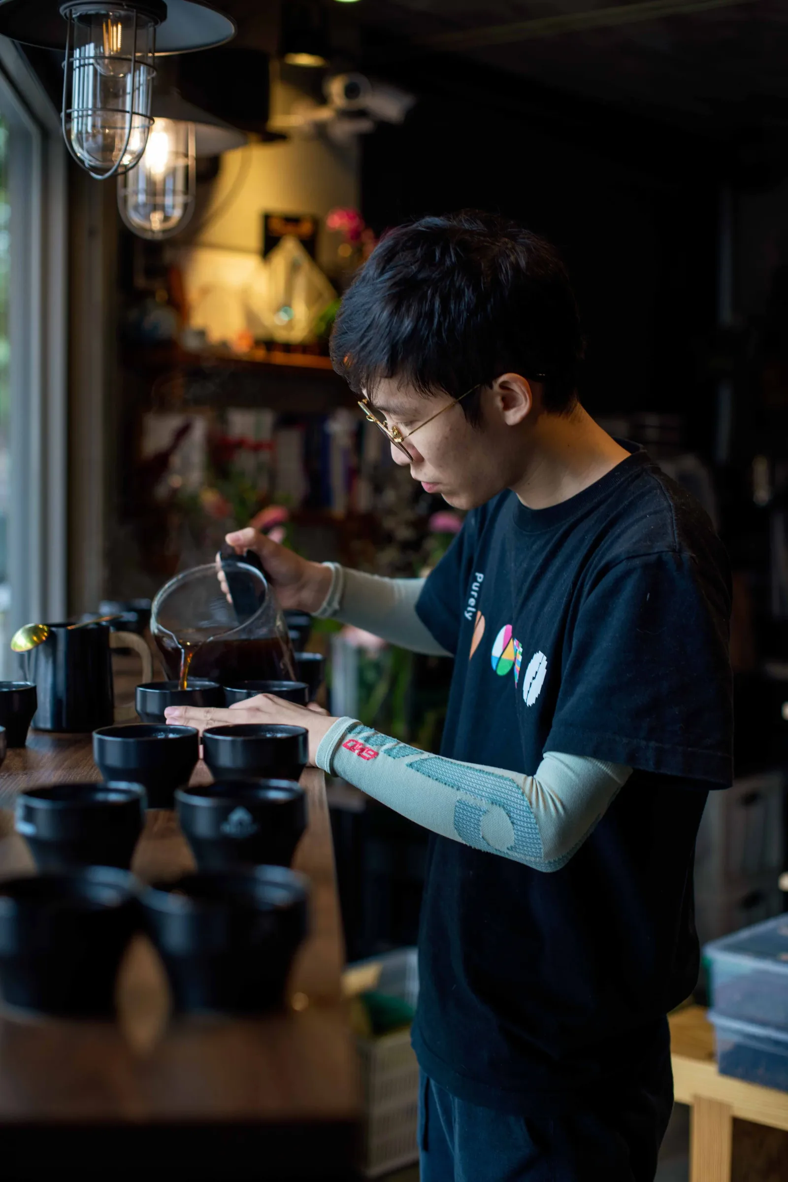 young person in glasses pouring tea into black ceramic cups at night., bo coffee roaster, taipei