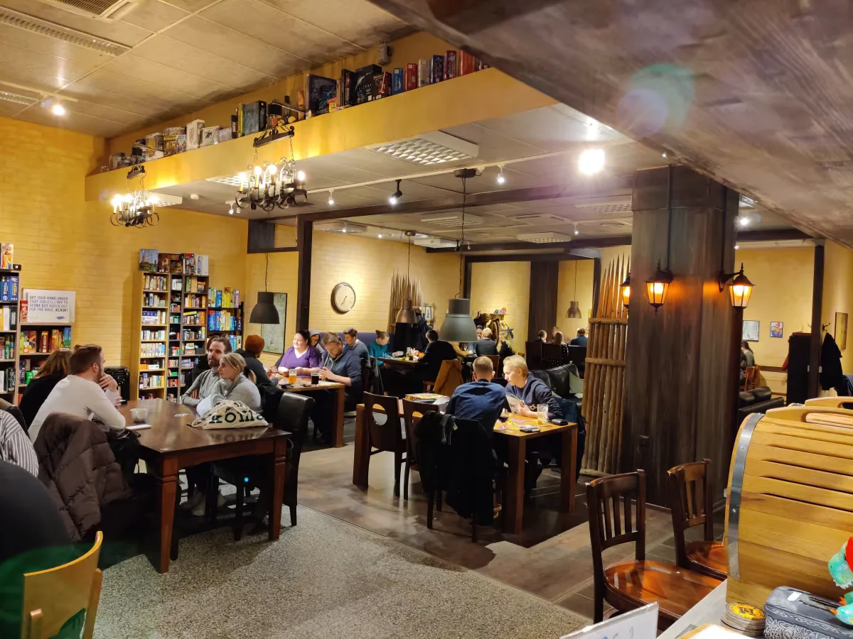 cozy café with yellow walls, bookshelves, patrons dining at wooden tables., board game cafe taverna, tampere