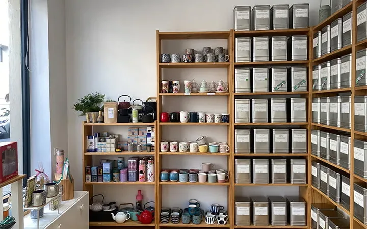 organized wooden shelving displays tea canisters, teapots, and ceramic vessels., botanic café en grano y tienda de té, valenc