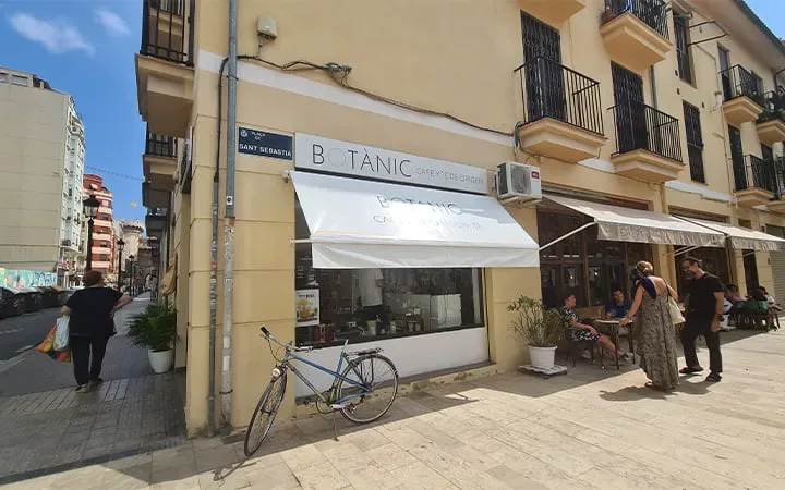 street-level boutique storefront with awning, bicycle parked outside, pedestrians nearby., botanic café en grano y tienda de 