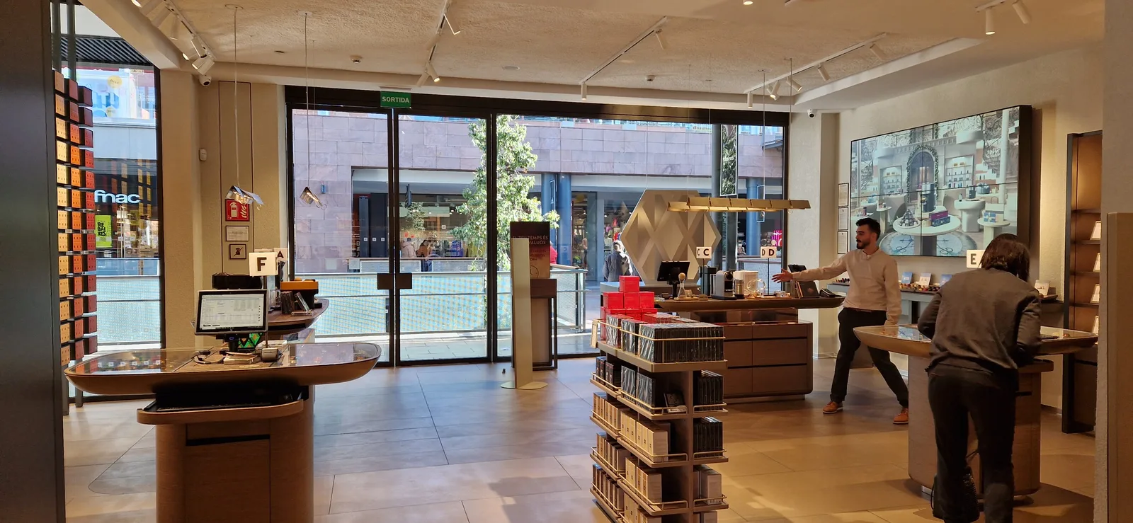 modern retail store interior with wooden displays, customers, and street-facing windows., boutique nespresso la maquinista, b