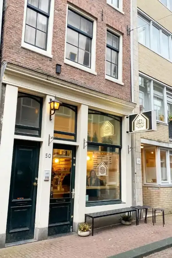 brick storefront with large windows, yellow lantern, and street-level seating bench., breadwinner - jordaan, amsterdam