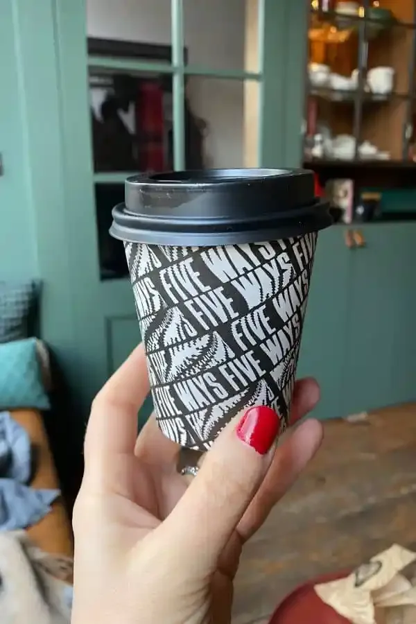 hand holding takeaway coffee cup with black lid and patterned sleeve in home interior., breadwinner - jordaan, amsterdam