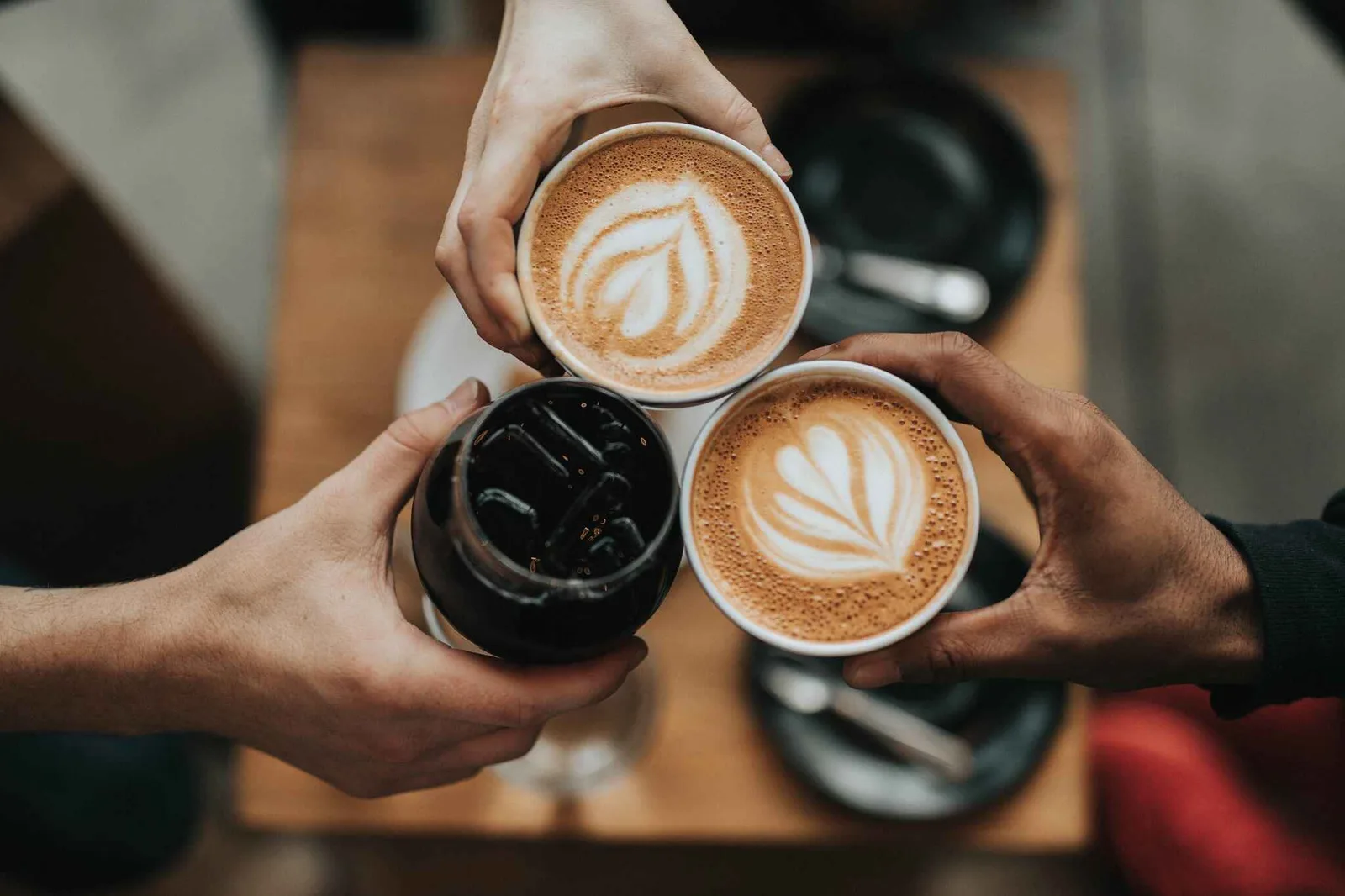 two hands holding three coffee cups with latte art designs displayed together., brisk coffee co, florida