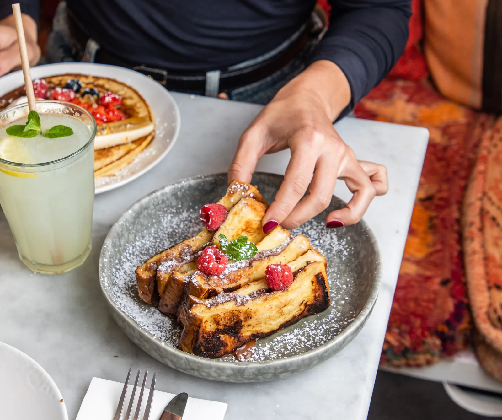 person enjoying french toast with berries, powdered sugar, and refreshing lemonade beverage., brother sister brunch lunch din