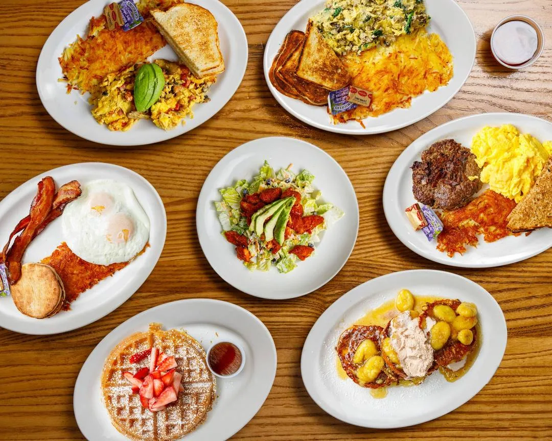 seven white plates with various breakfast and brunch dishes on wooden table., brothers cafe, san francisco