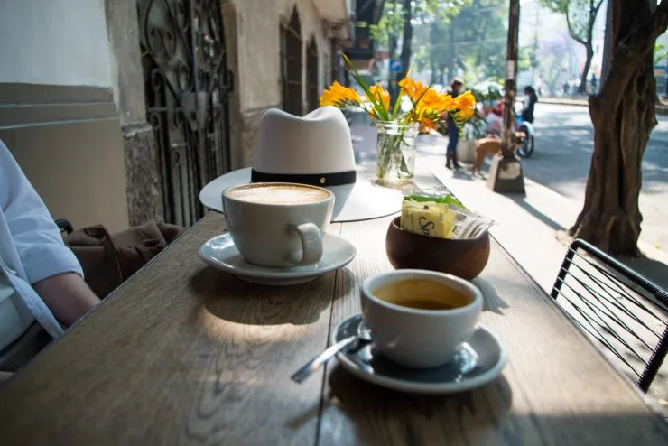 outdoor café table with coffee cups, white hat, and yellow flowers in vase., café almonte, coyoacán, mexico city