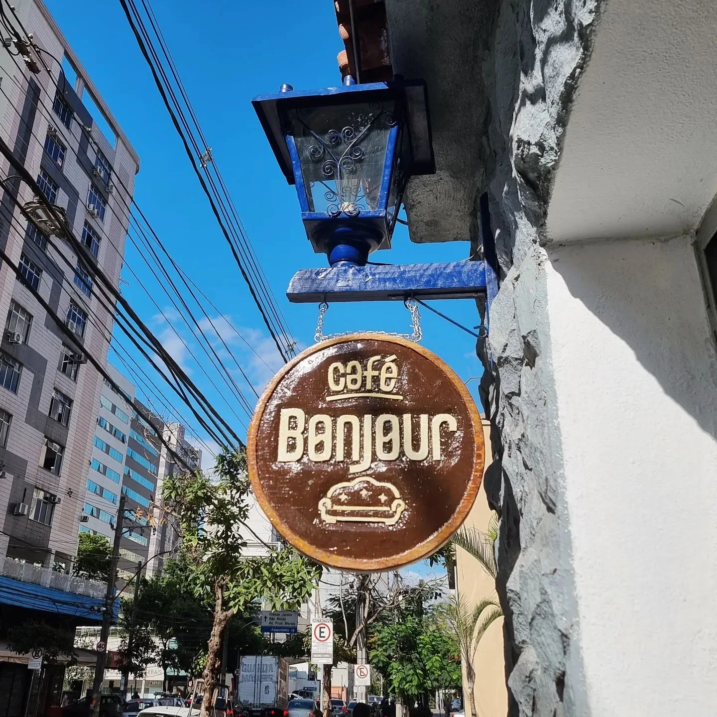 vintage brown circular cafe sign reading "bonjour" hanging from ornate blue bracket., café bonjour, belo horizonte
