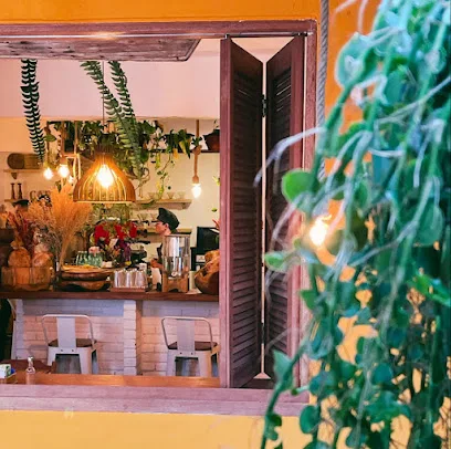 cozy storefront window display with plants, warm lighting, and indoor seating area visible., café da carol, rio de janeiro