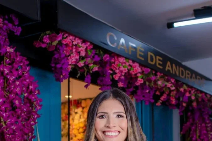 woman smiling in front of "cafe de andrade" storefront with vibrant magenta flowers., café de andrade - cafeteria no sudoeste